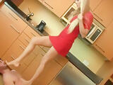 Blonde housewife in red dress tramples her handsome male slave in the kitchen